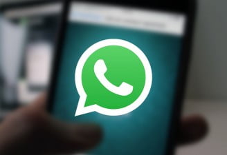 A photo of WhatsApp running on a phone in the background, a featured image for WhatsApp Beta gets forward counter with WhatsApp icon